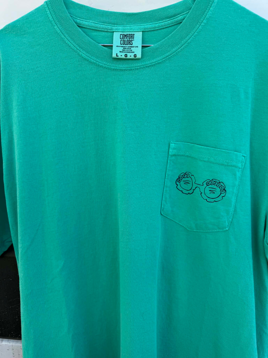 Green t-shirt with a pocket design and 'Comedy Colors' label on a white background