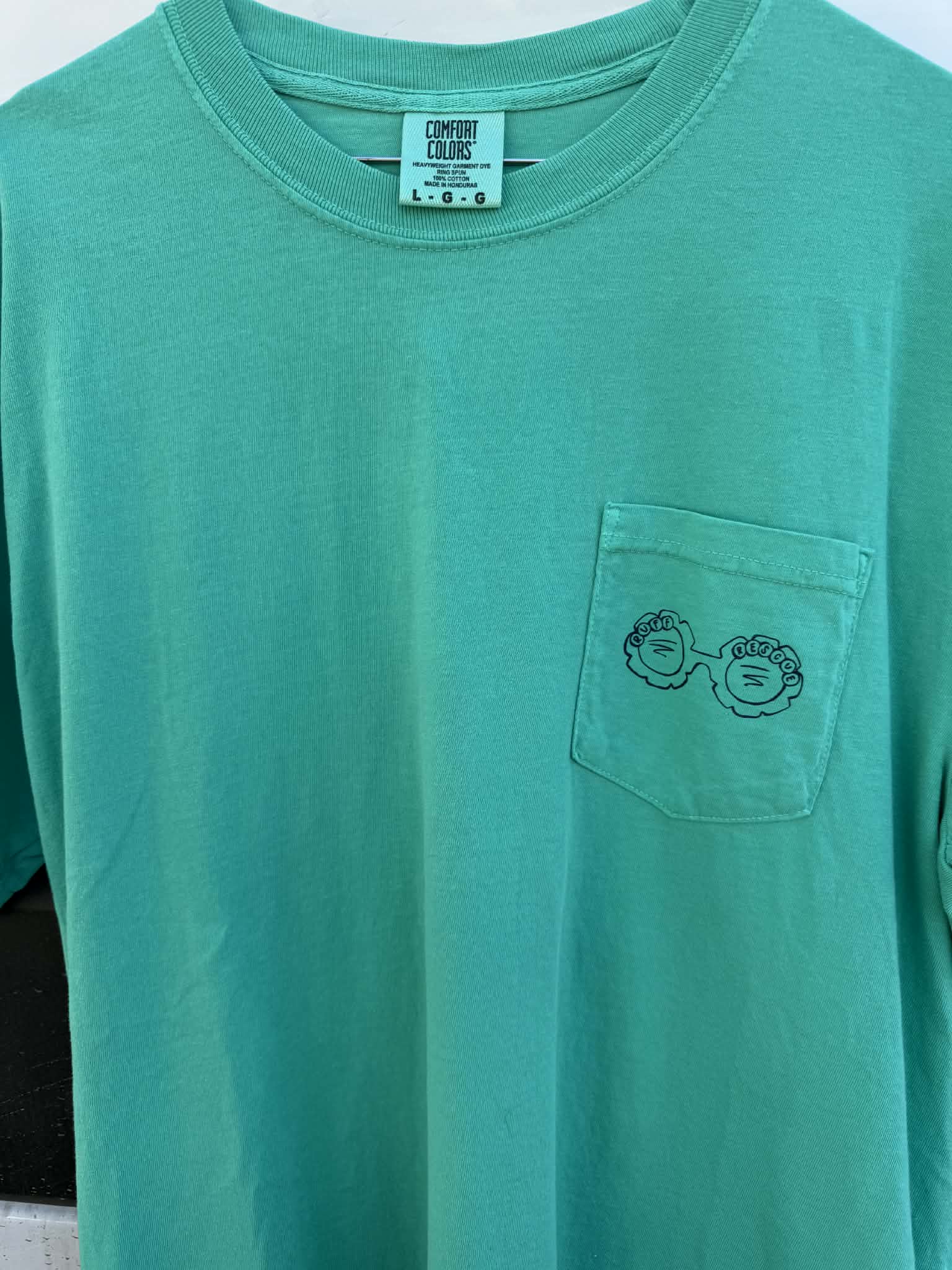 Green t-shirt with a pocket design and 'Comedy Colors' label on a white background